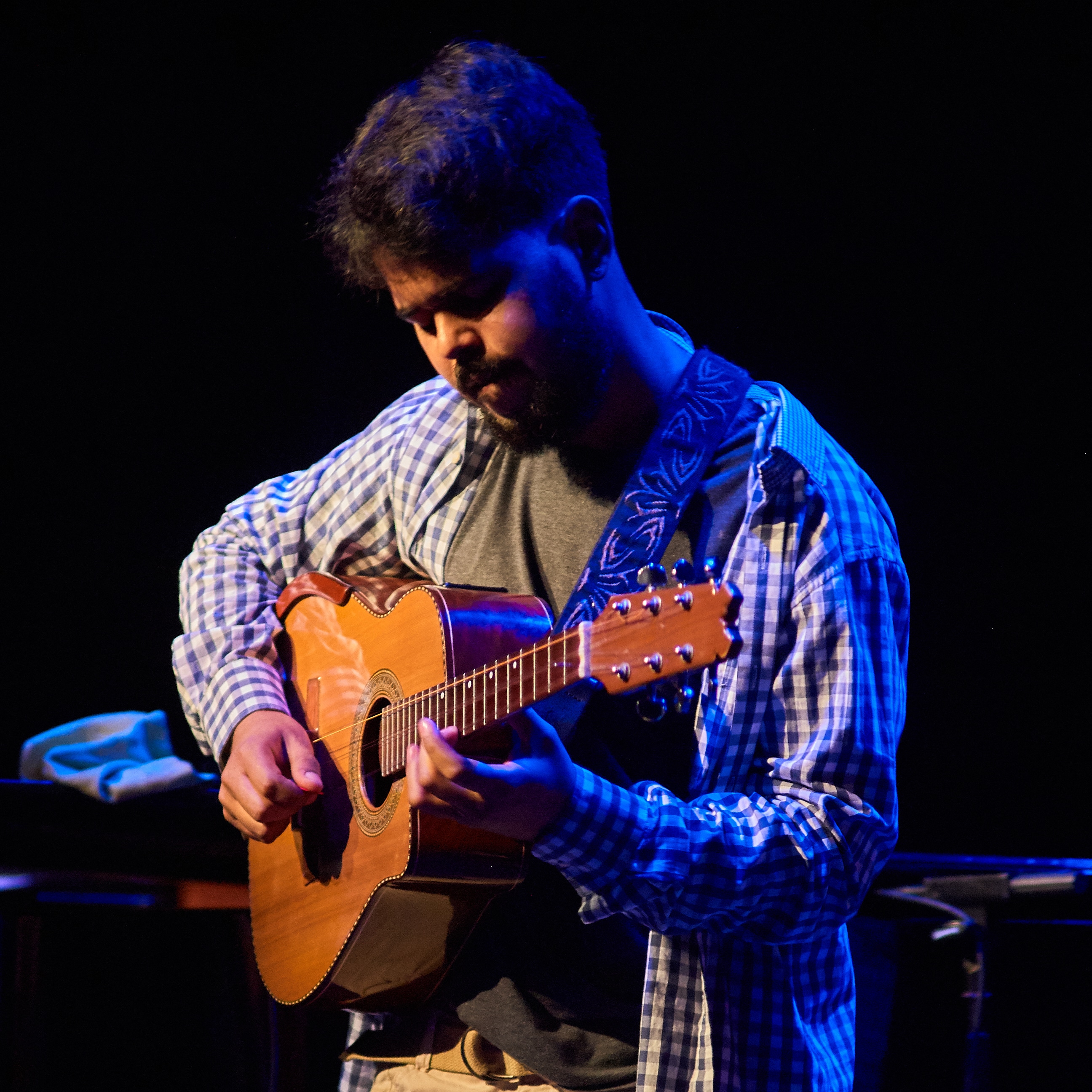 Mario Salvador playing the Cuban tres on stage under blue light
